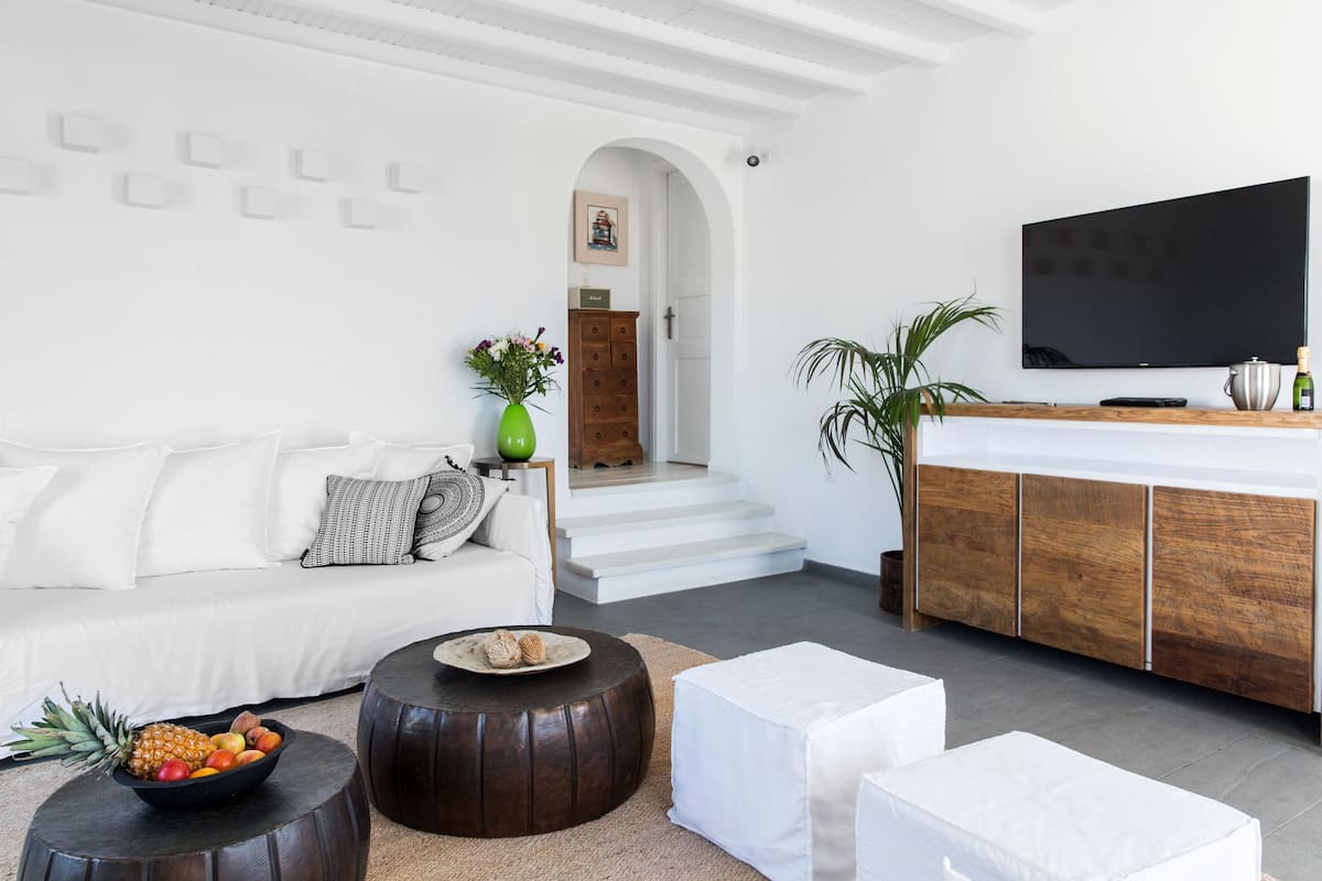 Una sala de estar moderna con un sofá blanco, una mesa de centro con fruta, un televisor y un mueble de madera.