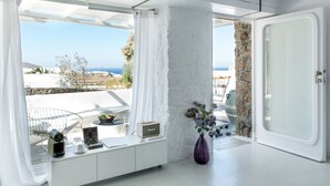 Una habitación moderna con decoración blanca, un ventanal con vistas al mar, un pilar de piedra y una puerta.