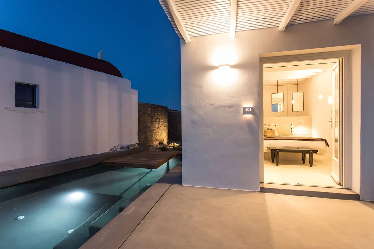 Exterior moderno de un hotel con piscina, entrada bien iluminada y baño visible con cama.