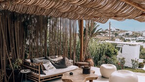 Un rincón exterior acogedor con un toldo tejido, un sofá con cojines y una mesa de centro de madera.