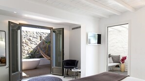 Un dormitorio moderno con una cama grande, una mesita redonda pequeña, una silla, un televisor y vistas a un muro de piedra exterior y una hamaca.