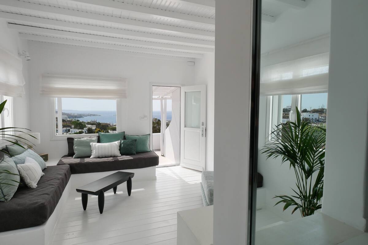 Una sala de estar moderna con un gran ventanal que ofrece vistas al mar y edificios.