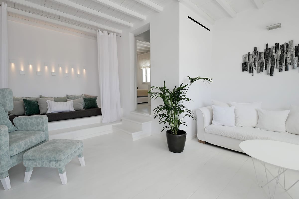Una sala de estar moderna con un sofá, un sillón y un reposapiés, una planta en maceta y una mesa de centro blanca.