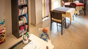 A room with a dining table, chairs, a bookshelf, and a small table with a drawing and toys. - Kyriad Toulouse Blagnac Aéroport (Blagnac)