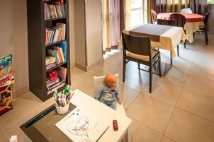 Una habitación con una mesa de comedor, sillas, una estantería y una mesita con un dibujo y juguetes.