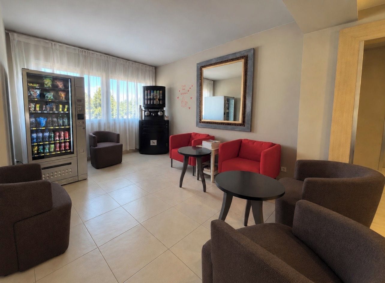 Ein Hotelzimmer mit Sitzgelegenheit, einer Kaffeemaschine und einem Getränkeautomaten.