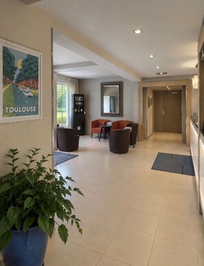 A hotel lobby with a reception desk, seating area, and a large potted plant. - Kyriad Toulouse Blagnac Aéroport (Blagnac)