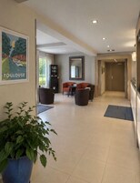 Un vestíbulo de hotel con una recepción, zona de asientos y una planta grande en maceta.