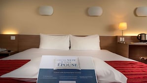 Een hotelkamer met een netjes opgemaakt bed, een nachtkastje met een lamp en een wandlamp.