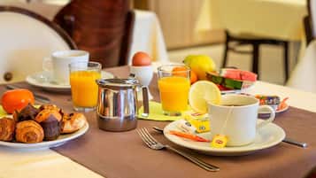 Mesa de café da manhã com croissants, suco de laranja, café e uma tábua de frutas.