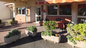 Een terras met zitgedeelte, plantenbakken, een overdekte patio en een gebouw met een pannendak.