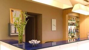 Een receptie met een balie, een wandklok, een prikbord en een glazen vitrine met flessen.