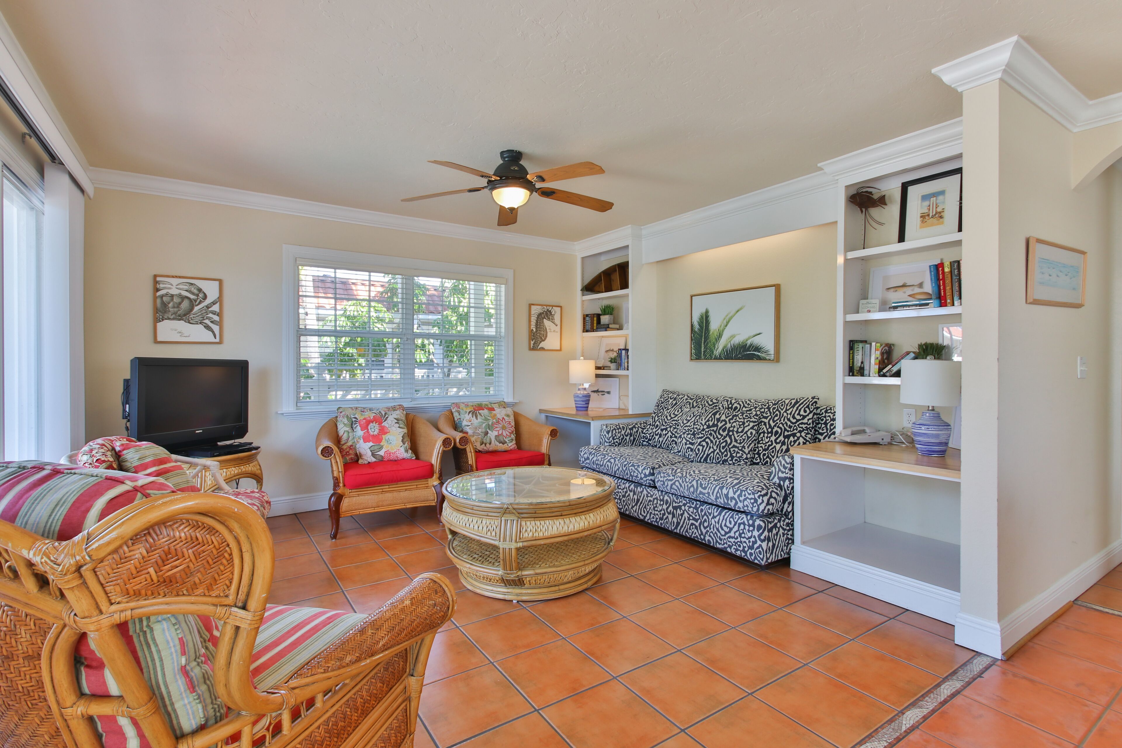 A living room with wicker furniture, a television, and a ceiling fan.