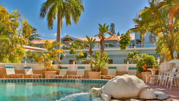 A pool area with lounge chairs, a large turtle sculpture, and a building with a red roof in the background.