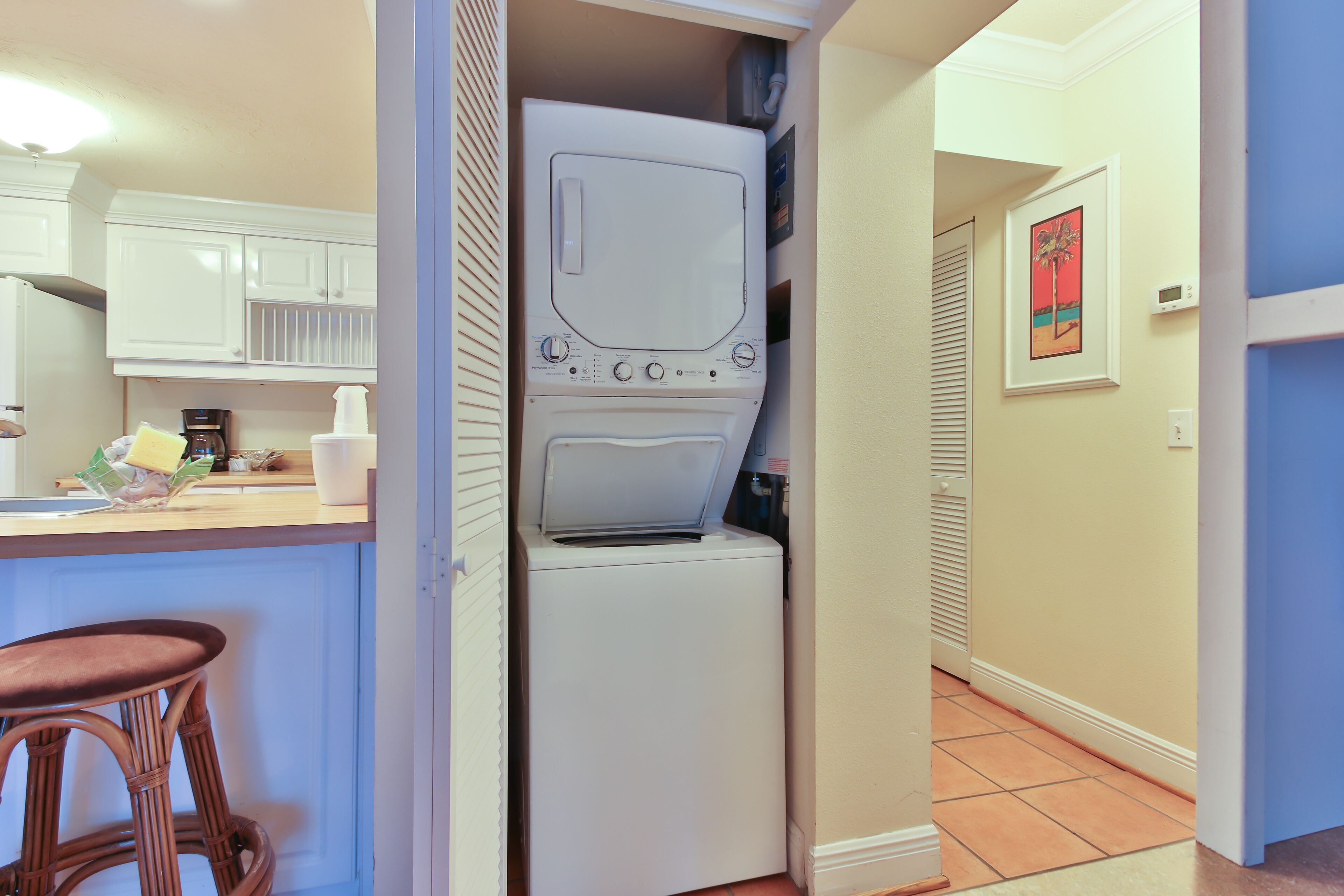 A compact kitchen with a built-in washer and dryer, a bar stool, and a coffee maker on the counter.