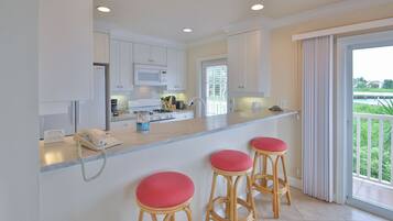 A modern kitchen with white cabinets, a microwave, and a gas stove. There are three wooden stools with red cushions. A phone is on the counter, and a window with blinds is visible.