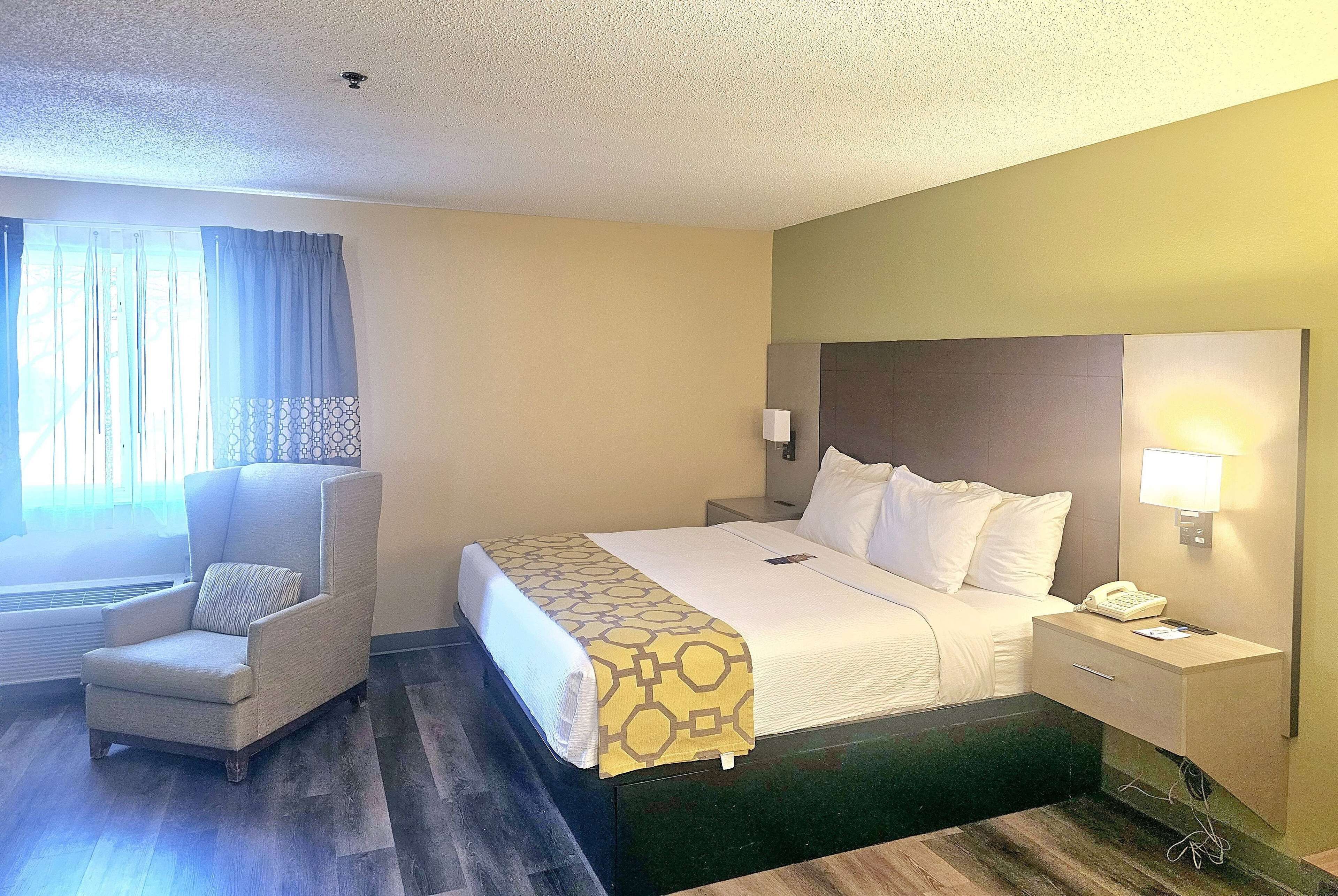 A hotel room with a bed, a chair, a nightstand, and a lamp.
