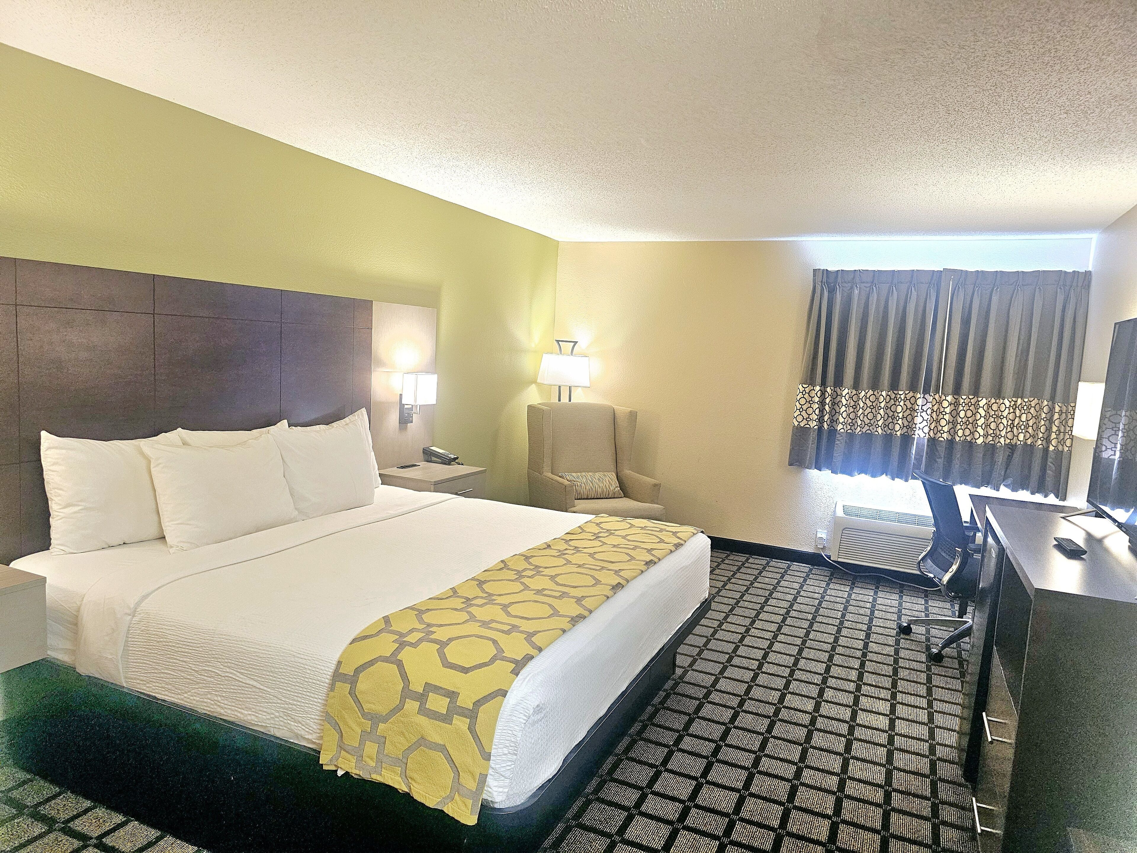 A hotel room with a bed, a chair, a desk, a lamp, and a television.