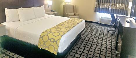 A hotel room with a bed, a chair, a desk, a lamp, and a television.