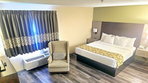 A hotel room with a bed, a chair, a bedside table, a nightstand, a wall-mounted lamp, and a window with curtains. - Baymont by Wyndham Rolla (Rolla)