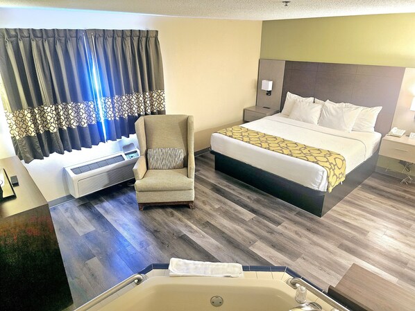 A hotel room with a bed, a chair, a bedside table, a nightstand, a wall-mounted lamp, and a window with curtains.