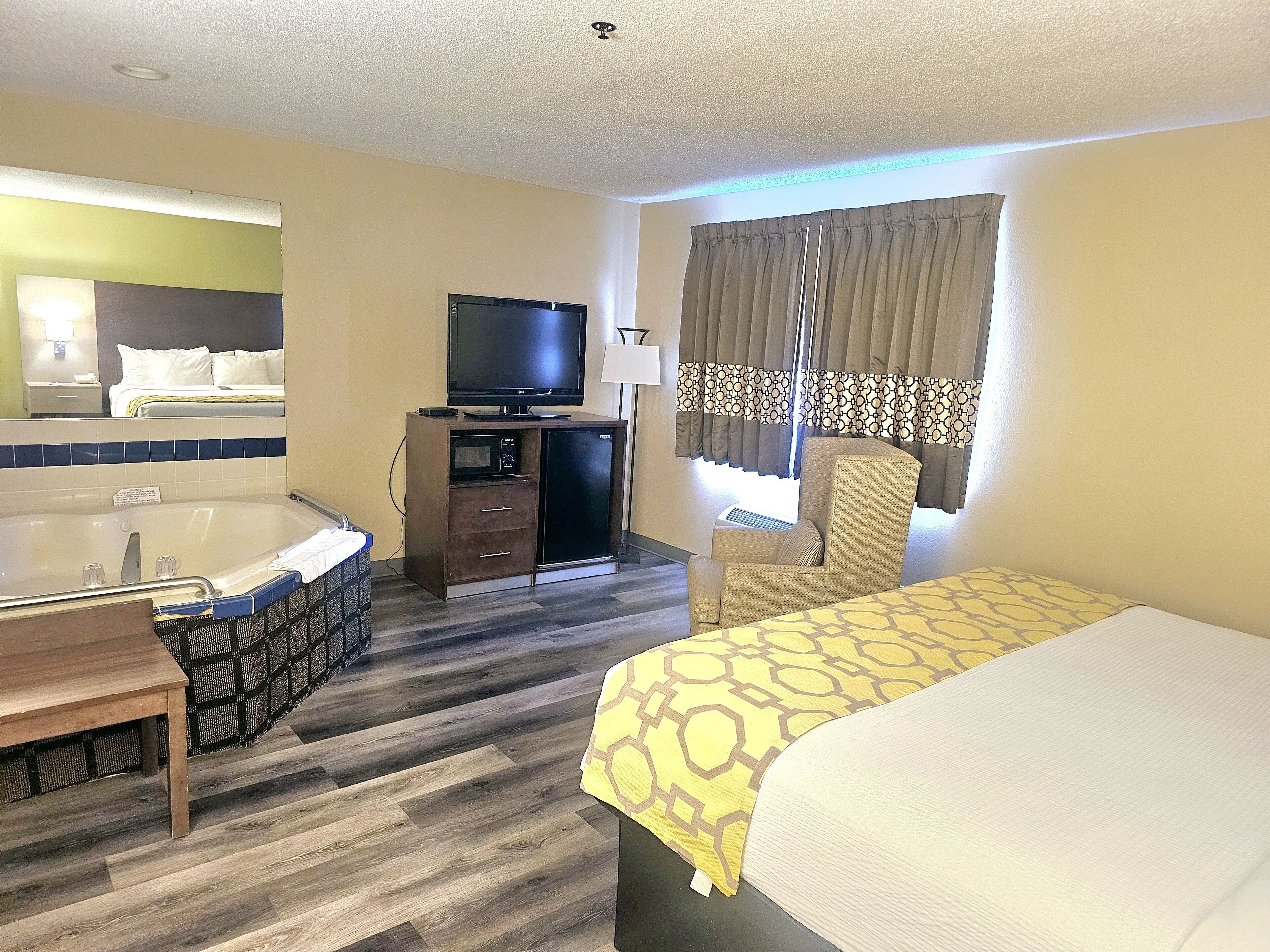 Une chambre d’hôtel équipée d’un lit, d’une chaise, d’un bureau, d’une télévision, d’un mini-bar et d’une fenêtre avec des rideaux.