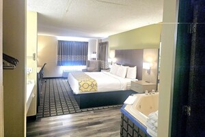 Habitación de hotel con una cama grande, mesitas de noche, un escritorio, una silla, un baño con bañera y una ventana con cortinas.