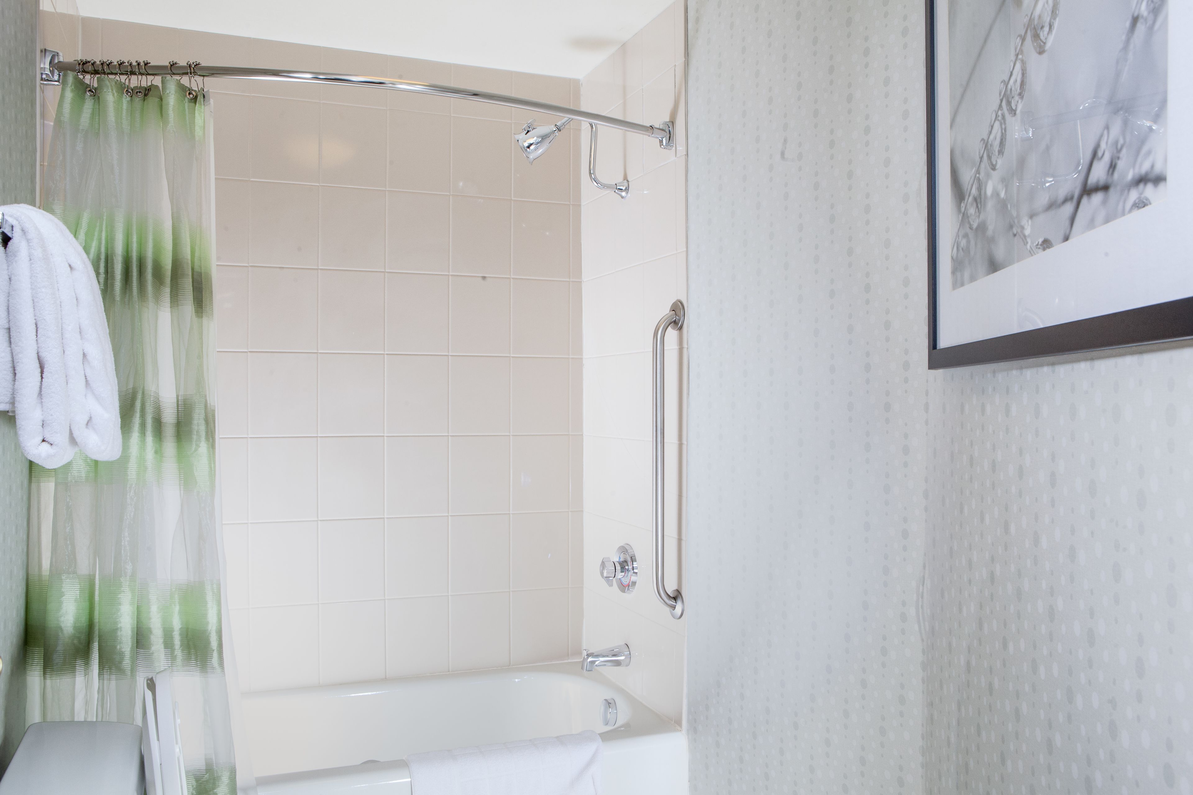 A modern bathroom with a bathtub, a shower curtain, and a handrail.