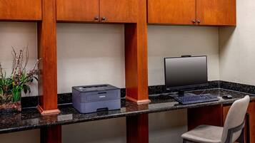 A workspace with a desktop computer, keyboard, and mouse on a granite countertop, under wooden cabinets.