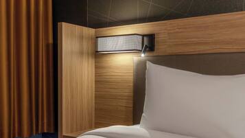 A hotel room with a bed, a headboard, a wall-mounted light fixture, and a curtain.
