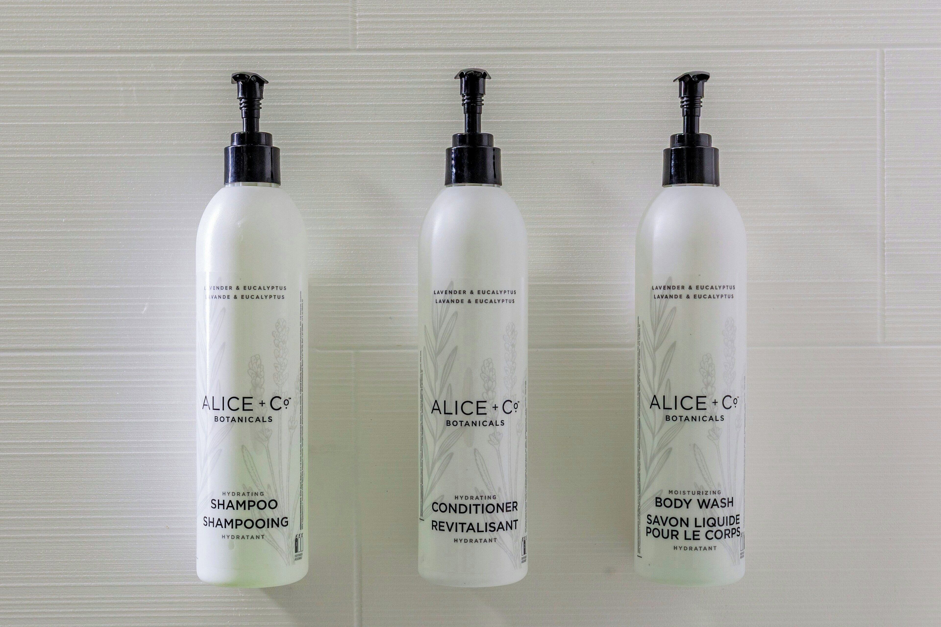 Tre bottiglie di prodotti Alice + Co Botanicals: shampoo idratante, rivitalizzante balsamo e detergente corpo.