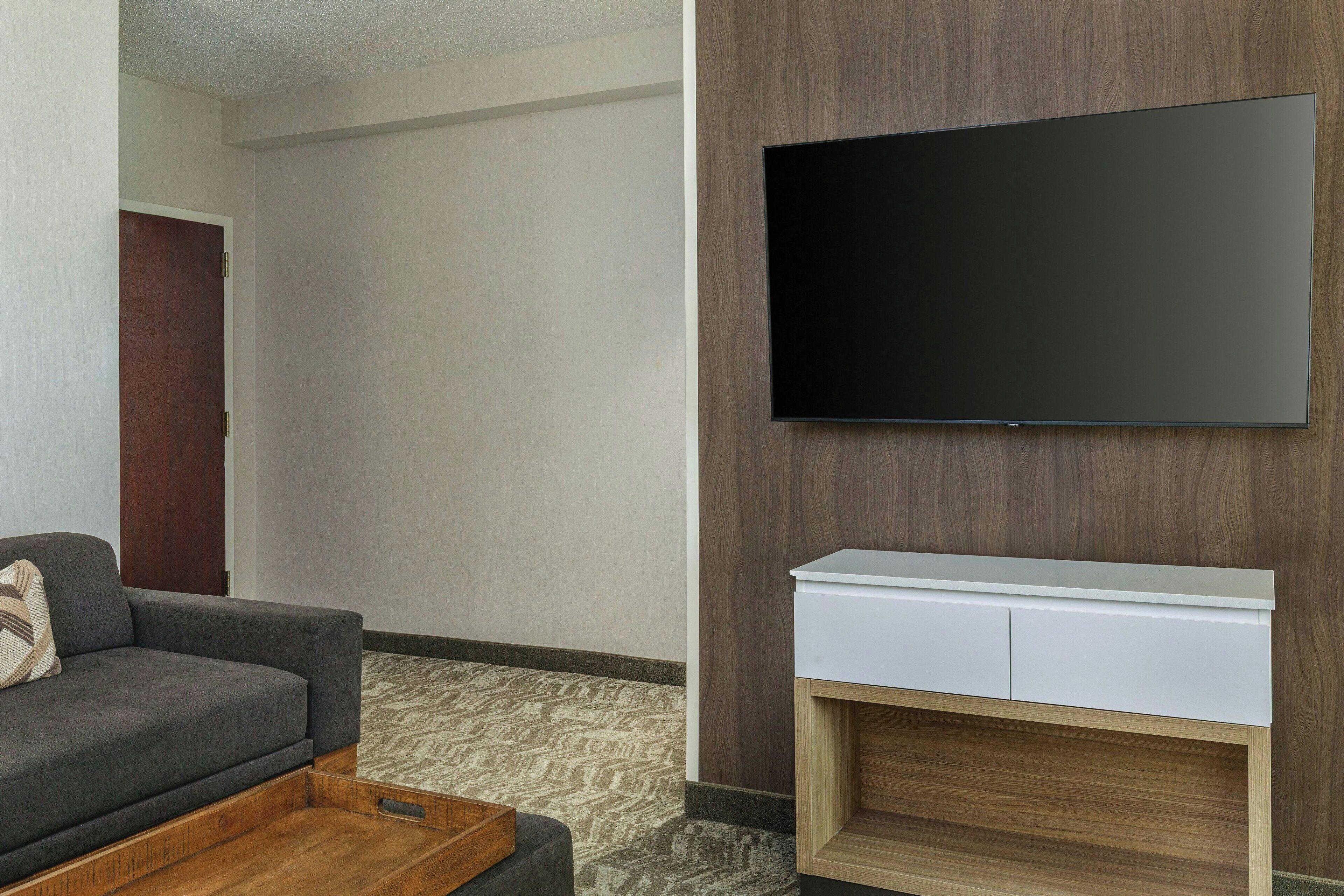 A modern living room with a flat-screen TV mounted on a wooden wall, a gray sofa, and a white console table.