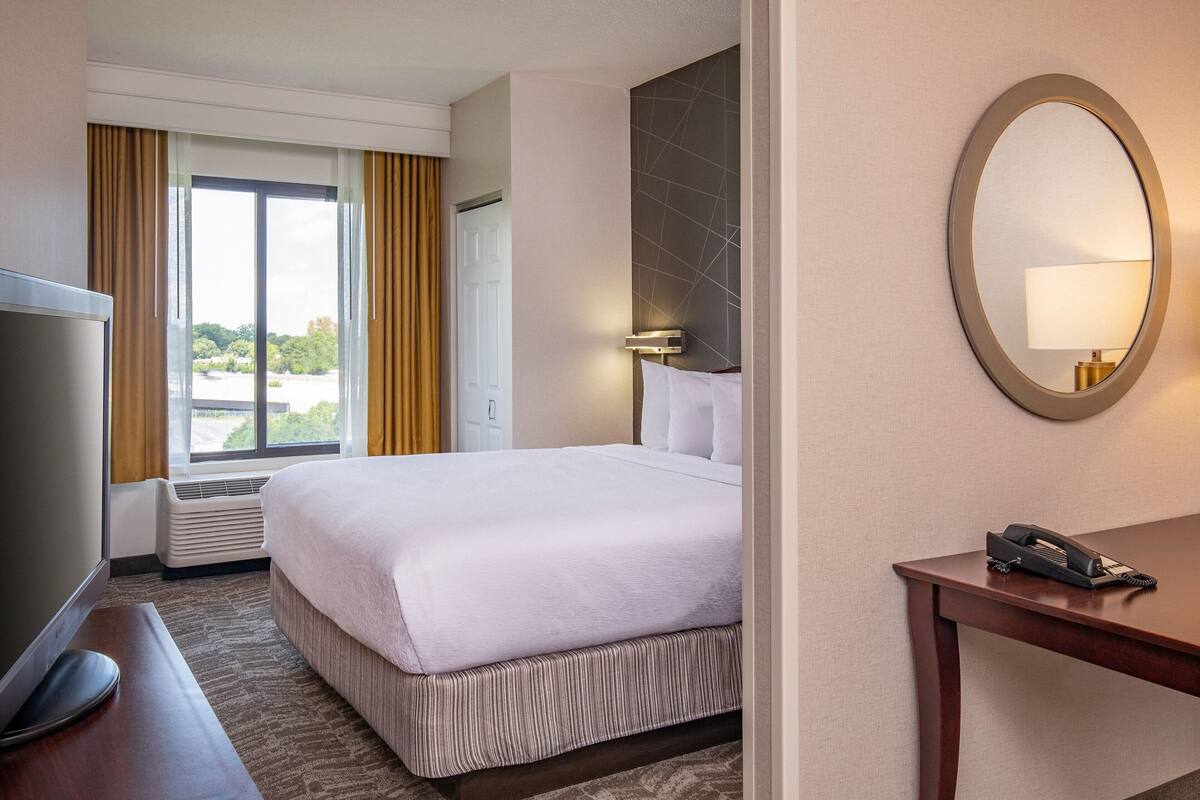 A hotel room with a large bed, a desk with a telephone, a TV, and a window with curtains.