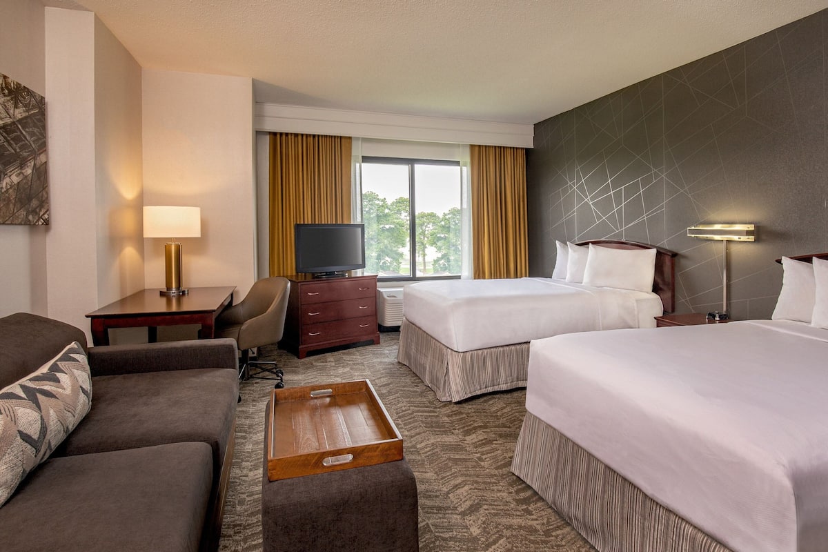 A hotel room with two beds, a sofa, a TV, a desk, and a window with curtains.