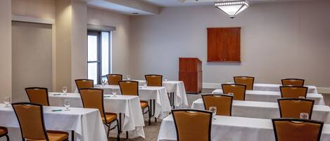 A conference room with multiple tables and chairs, a podium, and a large window.