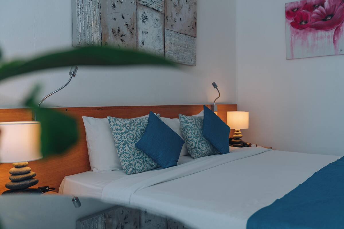 Cama bem arrumada com almofadas estampadas, cabeceira de madeira e abajur.