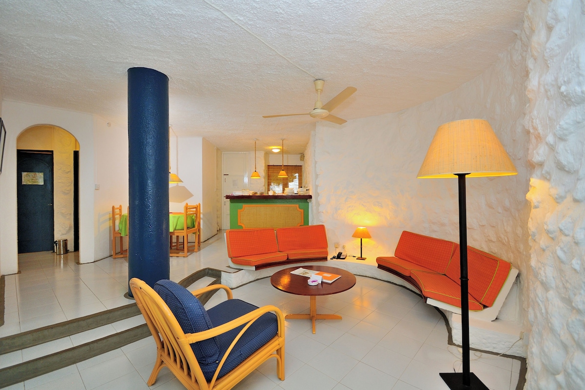 Un salon comprenant un canapé, un fauteuil et une table basse, ainsi qu’un ventilateur de plafond et une lampe.