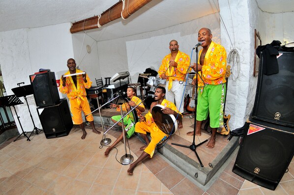 Un grupo de músicos tocando en una sala con suelo de baldosas, una batería y varios instrumentos musicales.