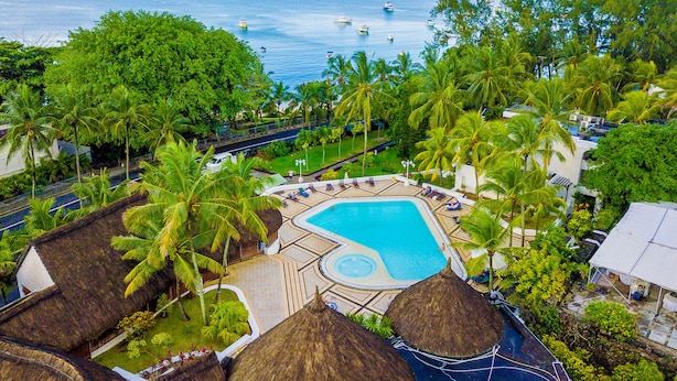 Un resort con piscina central, rodeado de palmeras y construcciones de techo de paja.