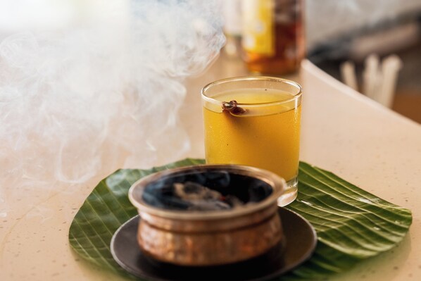 Un vaso de bebida amarilla sobre una hoja, un cuenco pequeño con tapa y una botella al fondo.