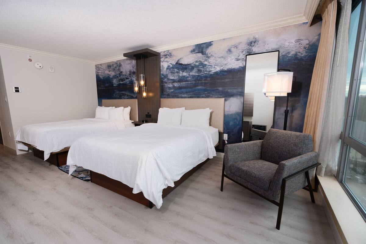 Une chambre d’hôtel avec deux lits, une chaise, un grand miroir et une fresque murale.