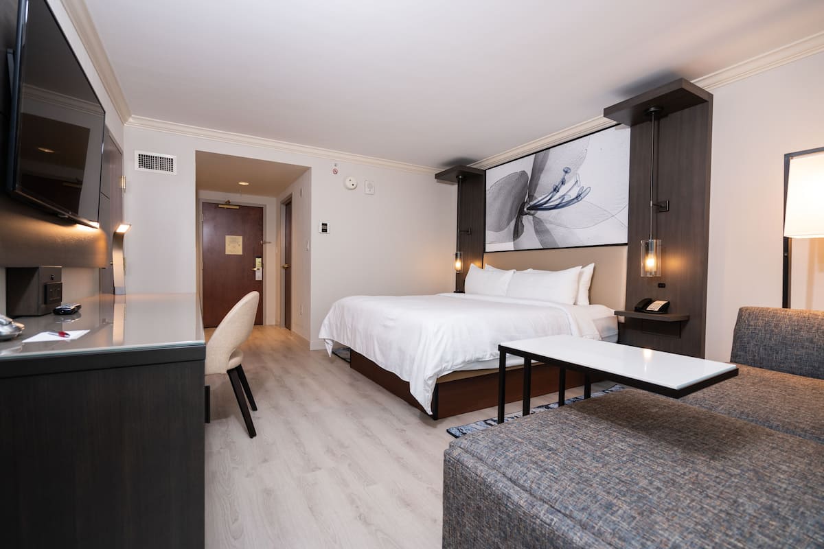 Une chambre d’hôtel comprenant un lit, un bureau, une chaise, un canapé et une grande œuvre d’art accrochée au mur.