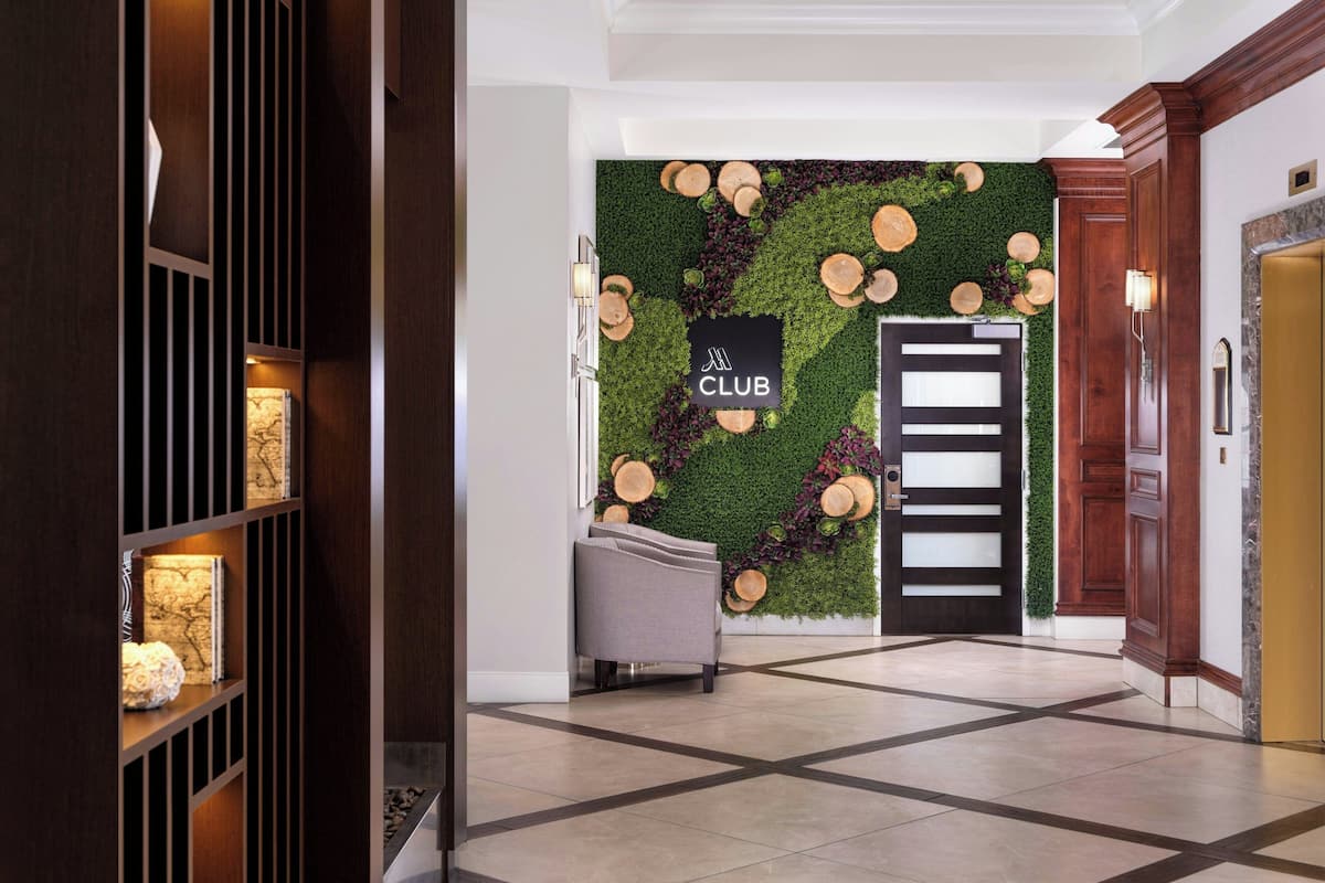Un hall d'hôtel moderne avec un mur végétal, une enseigne « CLUB », un comptoir d'accueil et une porte en bois.