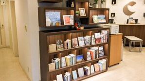 Uma livraria com prateleiras de madeira repletas de livros e objetos decorativos. Sinalizações indicam banheiros e há uma mesa de recepção ao fundo.