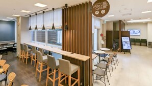 Um café moderno em uma biblioteca, com uma longa mesa de madeira, várias cadeiras e um amplo janelão.
