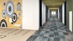 Um corredor comprido com carpete estampado, portas brancas e uma parede com desenhos circulares.