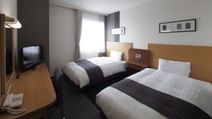 Quarto de hotel com duas camas, uma escrivaninha com telefone, televisão e cabeceira com painel de controle.