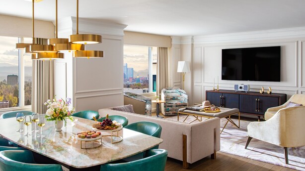 Et moderne hotelværelse med spiseplads, sofa, TV og udsigt over byen.