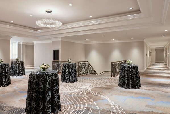 A spacious hotel lobby with a grand staircase, elegant chandeliers, and decorative tables with floral centerpieces.