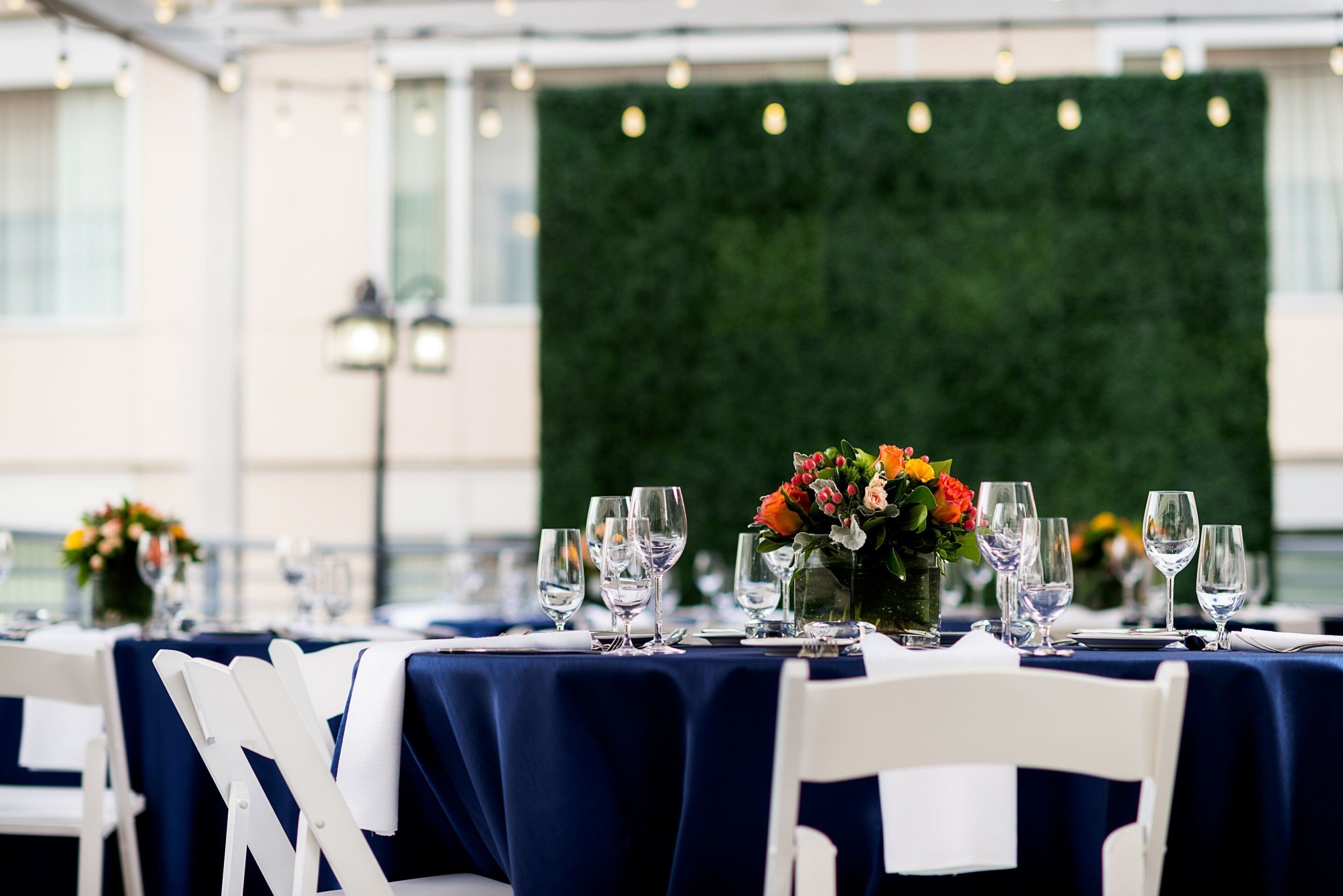 A table set for a formal event with a dark blue tablecloth, white chairs, and a floral centerpiece.
